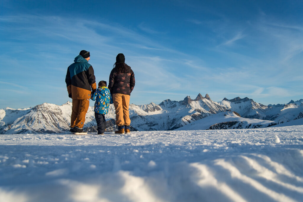 Photo prise de jour en format paysage, en hiver. Nous pouvons voir une famille qui observe les panoramas de La Toussuire. Au second plan nous pouvons voir les Aiguilles d'Arves