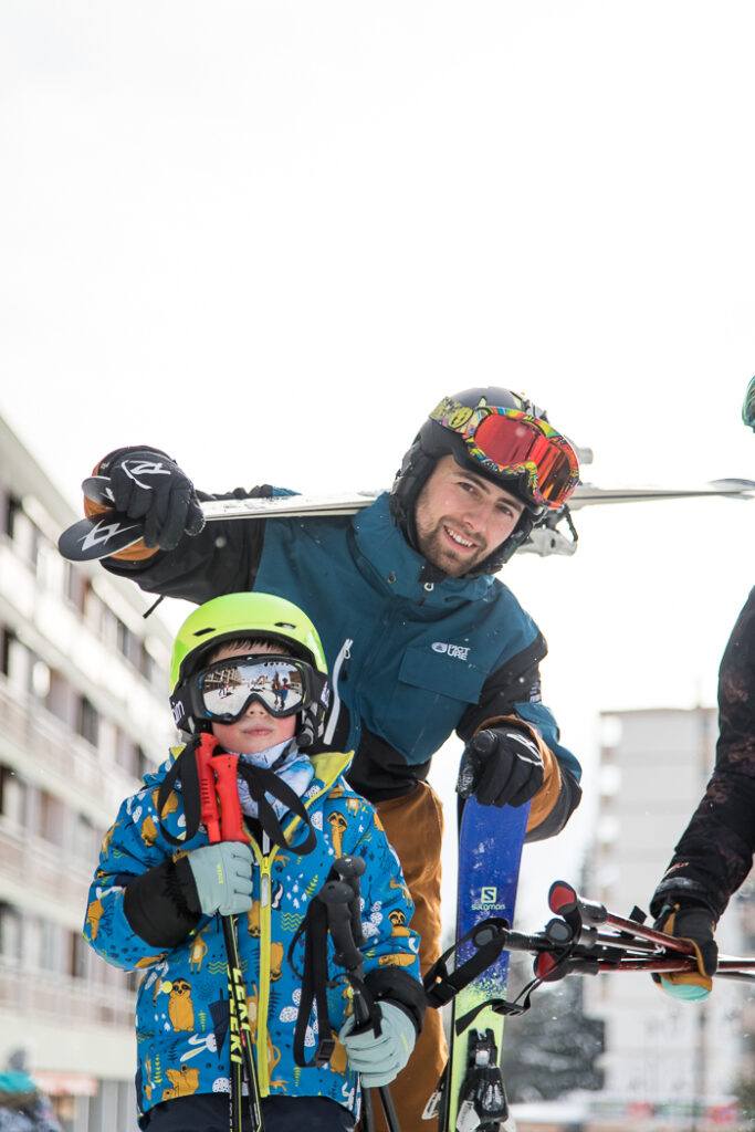 Winterportret overdag. We zien een vader en zoon op weg naar een ski-uitstapje. Ze kijken naar de fotograaf.  