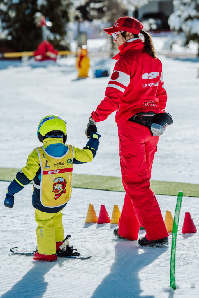 Portrait taken during the day in winter. We can see a ski instructor giving a lesson to a child. 