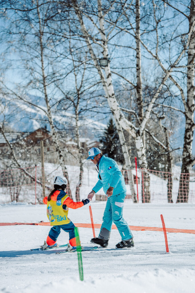Photo prise de jour en hiver en format portrait. Nous pouvons voir le jardin d'enfants de l'ESI l'école de ski internationale. Nous pouvons voir un enfant en cours de ski accompagner d'un moniteur.