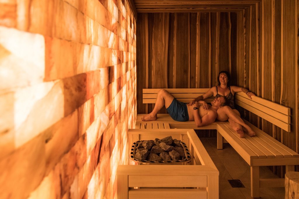 Couple allongé sur les bancs d'un sauna très lumineux avec des pierres chaudes au premier plan