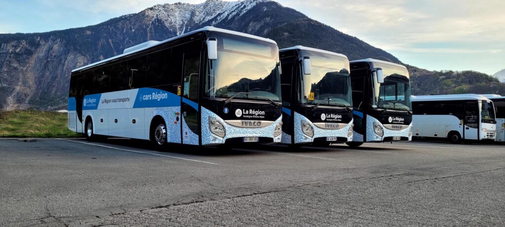 Foto genomen op een lentedag. We zien de bussen van Faure in driekwart-aanzicht met een berg op de achtergrond.