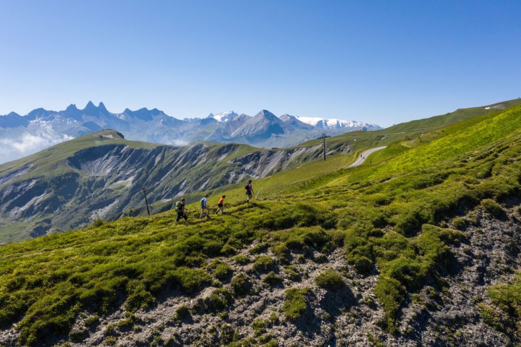 Image en drone où l'on voit une famille en randonnée sur les crêtes de la Toussuire ainsi que le paysage montagneux tel que les Aiguilles d'Arves.
