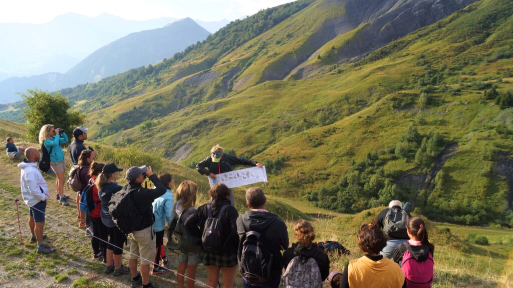 Guide de montagne en train d'expliquer les différentes types d'espèces sur le territoire devant un groupe de vacancier. Au second plan un paysage montagneux pour observer la nature