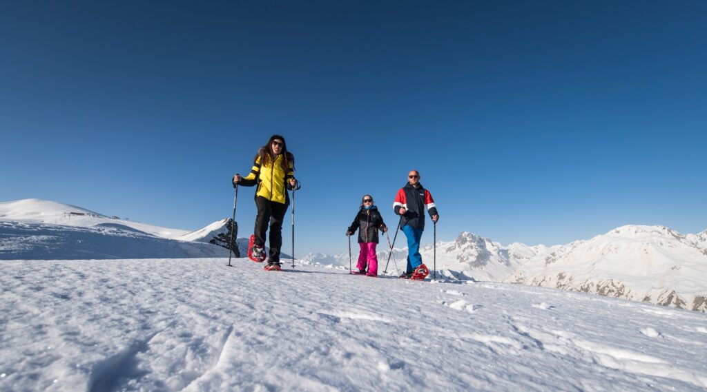 Een gezin probeert de sneeuwschoenen uit op de hoogten van La Toussuire in een besneeuwd landschap.
