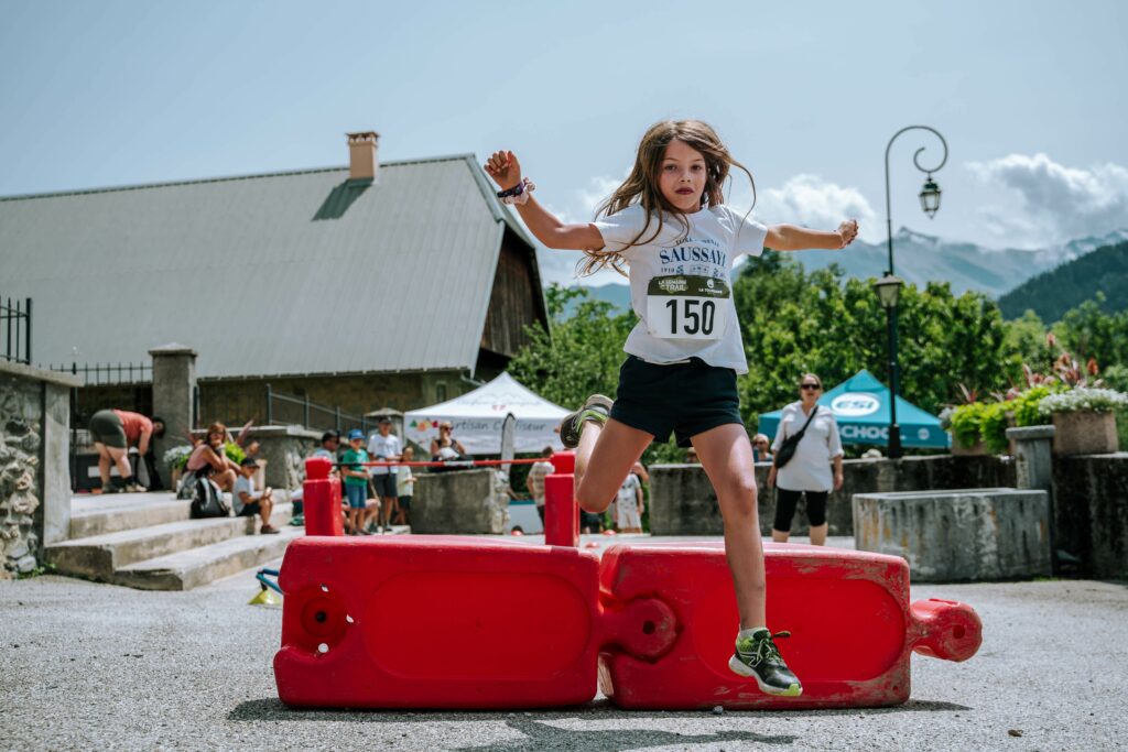 Photo prise de jour en format paysage. Nous pouvons y voir une enfant saut par dessus un obstacle. 