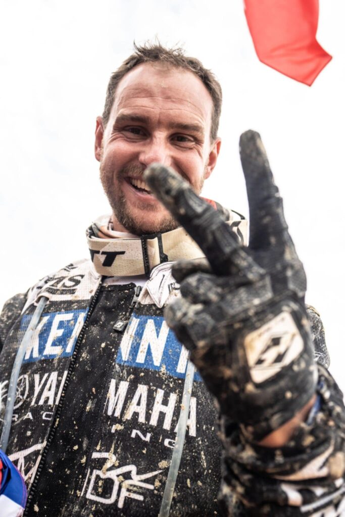 Alexandre Giroud, quadrijder, bedekt met modder, glimlachend en met zijn gehandschoende vuist in de lucht.