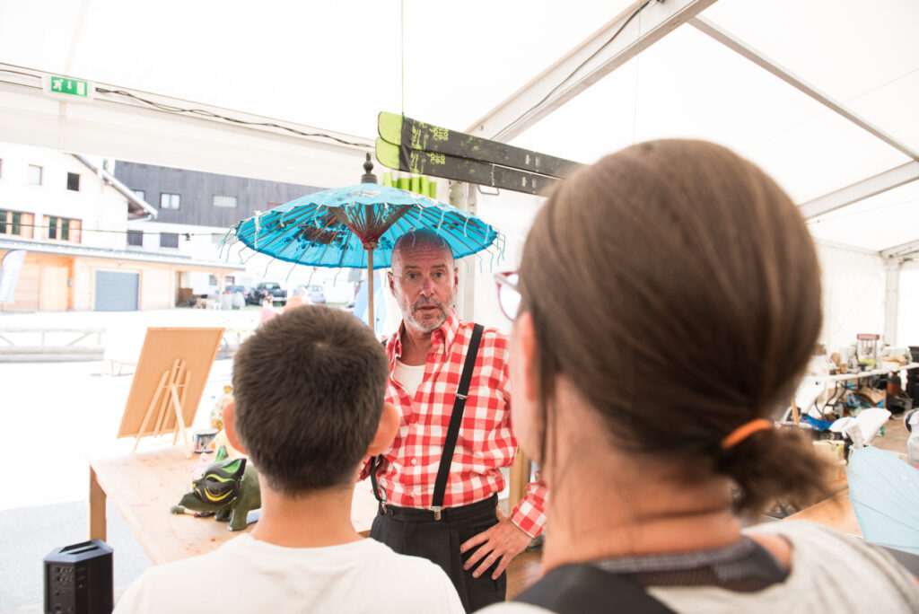 Photo prise de jour en format paysage. Nous pouvons voir deux enfants en train d'écouter une personne donner des conseils lors d'un atelier pendant le festival Le Spectacle Est Dans La Rue.