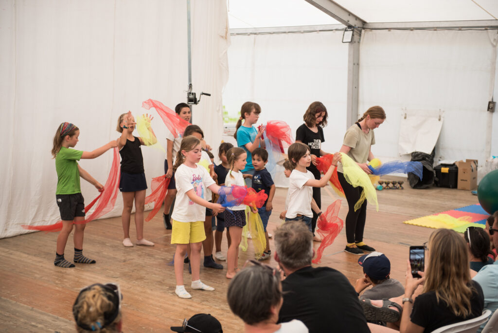 Photo prise de jour en format paysage. Nous pouvons voir un groupe d'enfants en train de faire un spectacle avec des foulards.