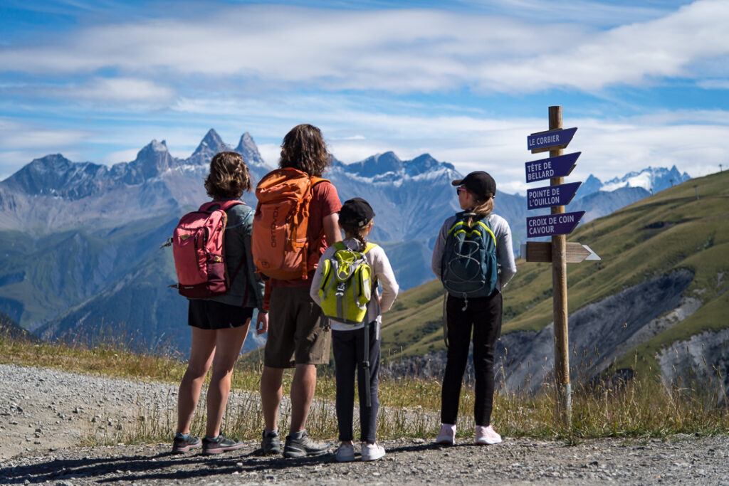 Photo prise en format paysage. La photo a été prise de jour en été. Nous pouvons voir une famille avec deux enfants en train de contempler les paysages. En arrière plan nous pouvons voir des montagnes, ainsi que les Aiguilles d'Arves.