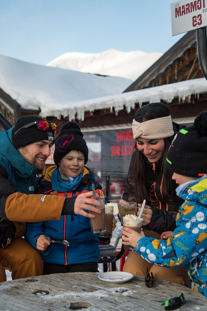Photo en format portrait de jour en hiver. Nous pouvons voir une famille de 4 personnes en train de boire des chocolats chauds.