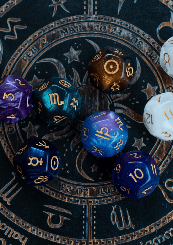Plusieurs dés à douze faces portant les symboles astrologiques (signes du zodiaque et planètes) posés sur un cadran représentant les signes, évoquant un outil de divination astrologique. Un atelier à découvrir lors de la Semaine Hygge – Bien‑être à La Toussuire.