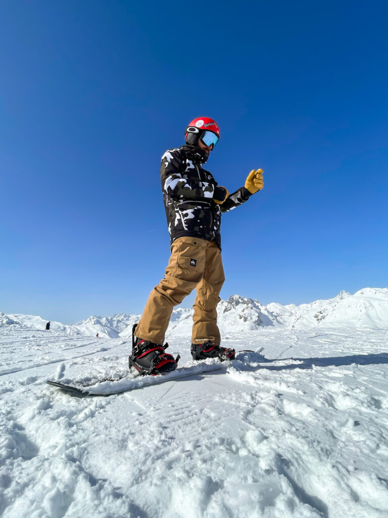 Photo prise de jour en format paysage en hiver. Nous pouvons un homme en snowboard en train de remettre ses gants.