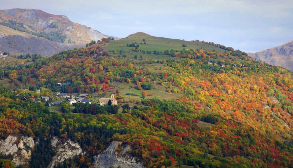Photo en format paysage pris de jour. Nous pouvons observer une montagne en automne avec les arbres qui ont les feuilles de couleurs différentes : vertes, jaunes, oranges, rouges.