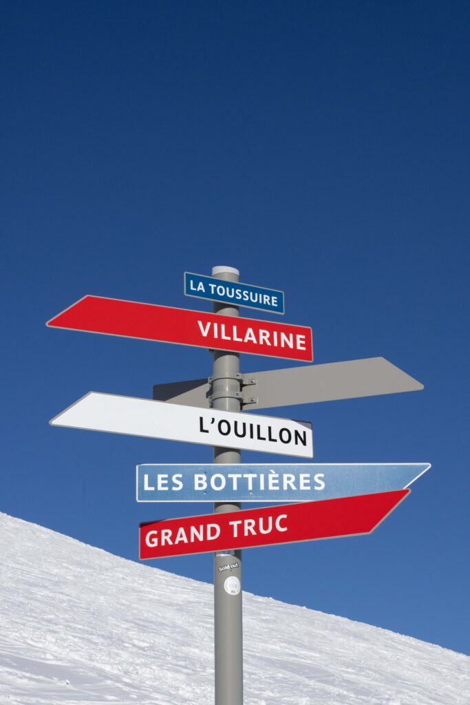 Photo prise de jour en hiver en format portrait. Nous pouvons voir un panneau directionnel de ski pour indiquer les différentes pistes.
