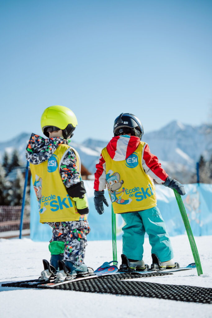 Photo prise de jour en format portrait en hiver. Nous pouvons voir deux enfants de dos pendant un cours de ski.