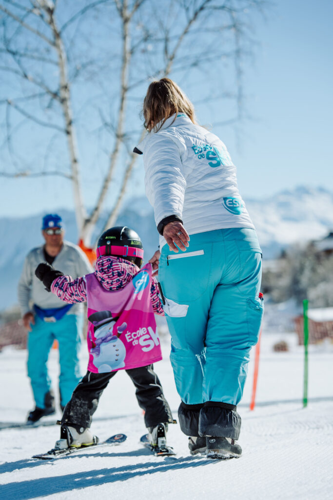 Photo prise de jour en hiver en format portrait. Nous pouvons voir le jardin d'enfants de l'ESI l'école de ski internationale. Nous pouvons voir un enfant en cours de ski accompagner d'une monitrice.