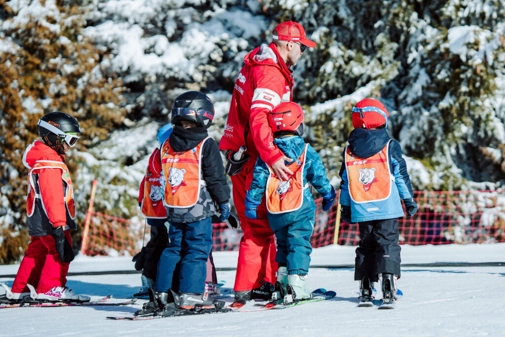 Photo prise en format paysage de jour en hiver. Nous pouvons voir un moniteur de ski en train de donner un cours à un groupe d'enfants.