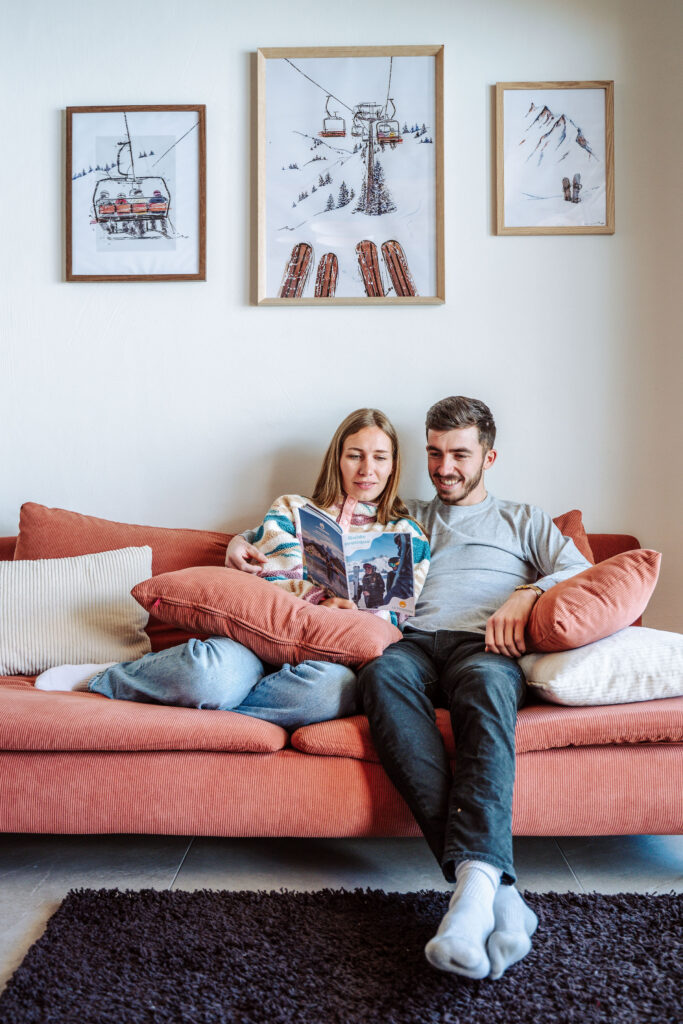 Photo prise de jour en format portrait en hiver. Nous pouvons voir un couple en train de lire une brochure de l'office de tourisme assis dans un canapé.