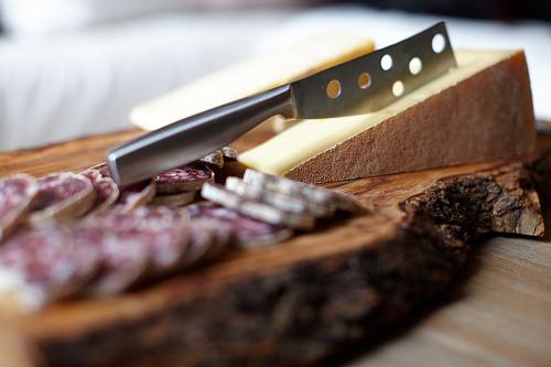 Photo d'un plateau de produits régionaux. nous avons des rondelles de saucissons ainsi qu'un morceau de Beaufort coupé avec un couteau sur une planche de bois