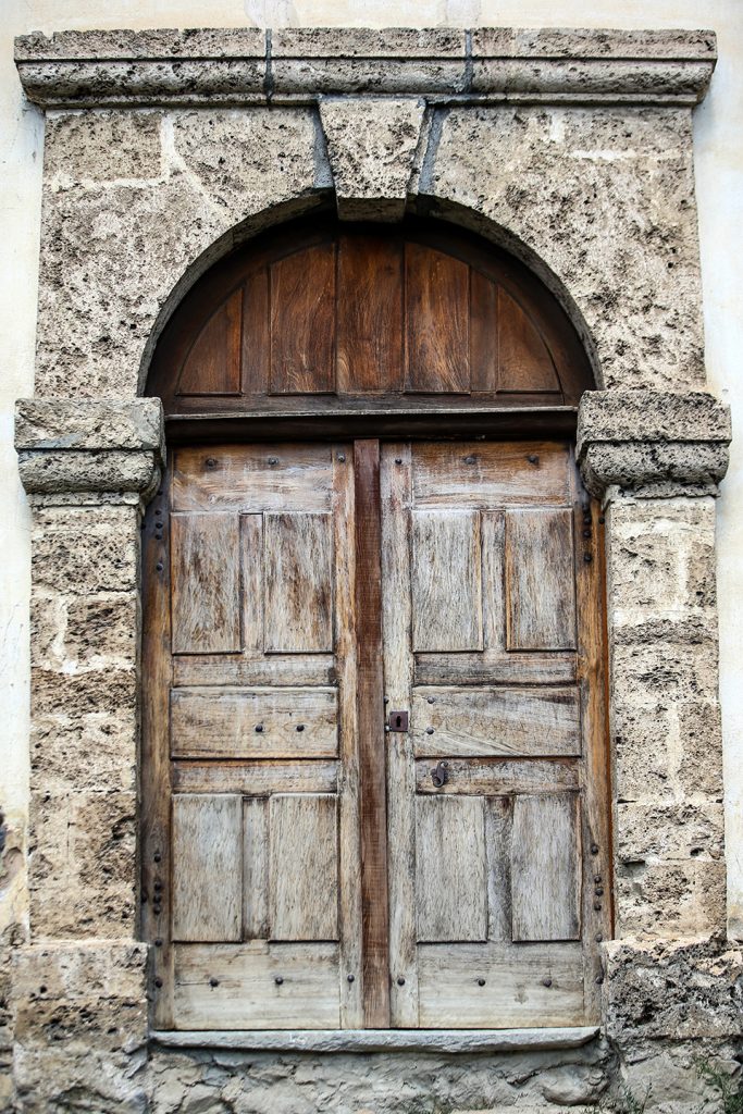 Detail of church front door. The door takes up all the space in the photo, which is centred. The double wooden door is surrounded by a stone arch.