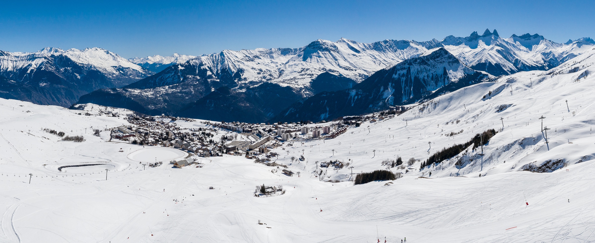Vue de La Toussuire en hiver depuis la Tête de Bellard. Découvrir la station dans la neige et les Aiguilles d'Arves à l'horizon.