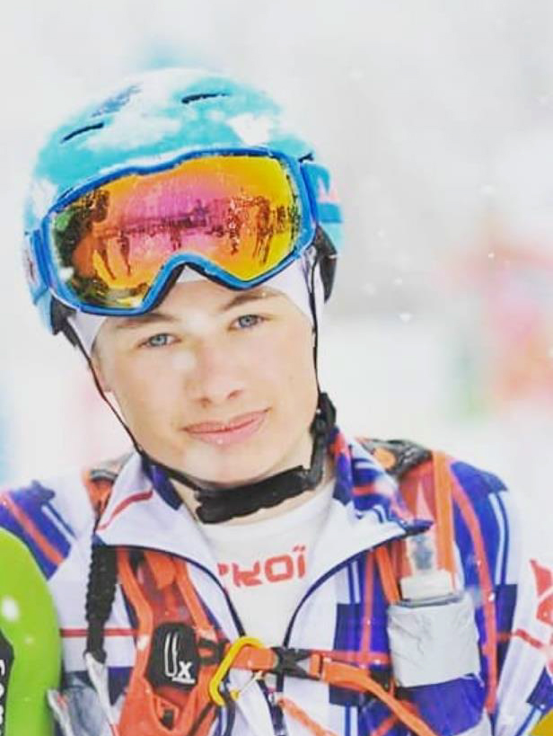 Foto genomen in de winter in verticaal formaat. We zien een portret van de jonge skiër Bastien Flammier in wedstrijdtenue met een helm en een masker