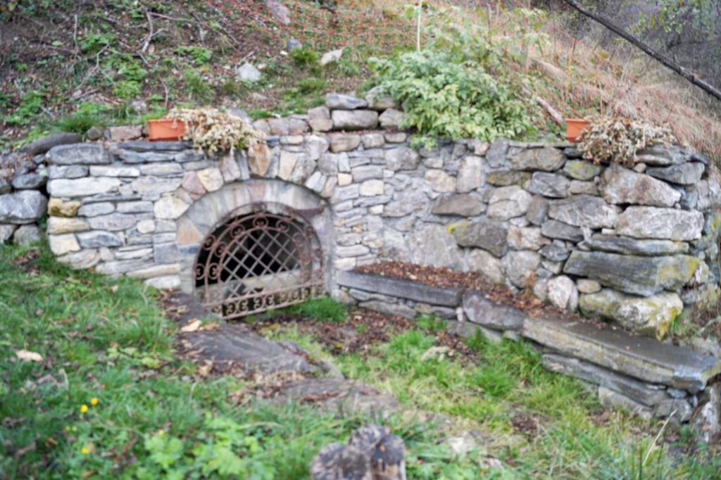 Foto van de overdekte fontein van Fontcouverte. We kunnen een rooster met een stenen muur zien waaronder een fontein rust