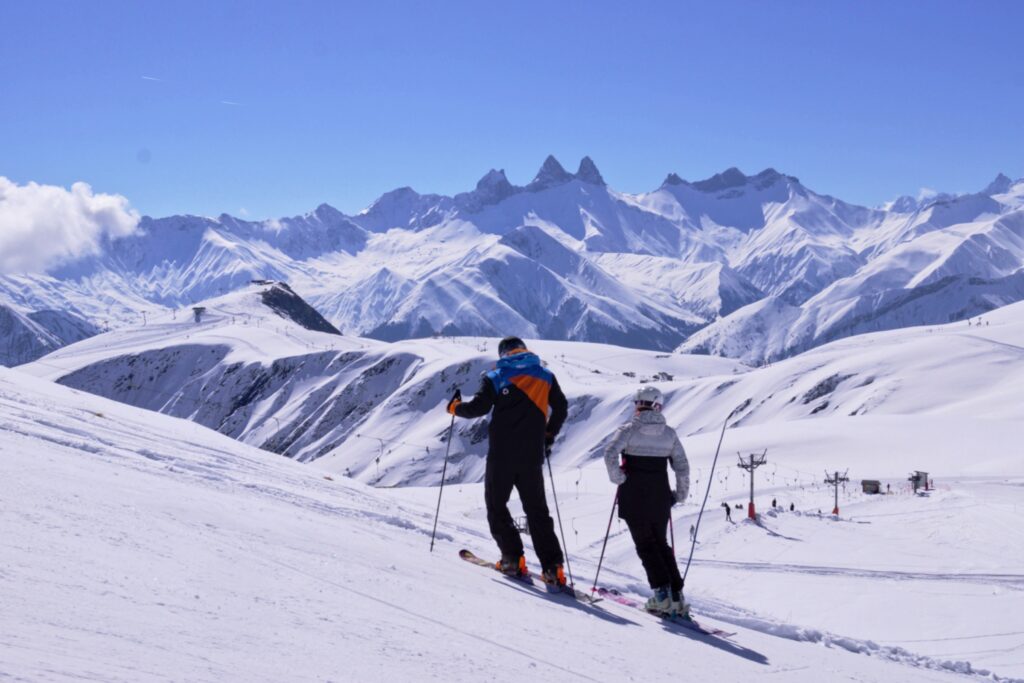 Un couple arrêté au bord d'une piste de ski admire le panorama des montagnes en second plan