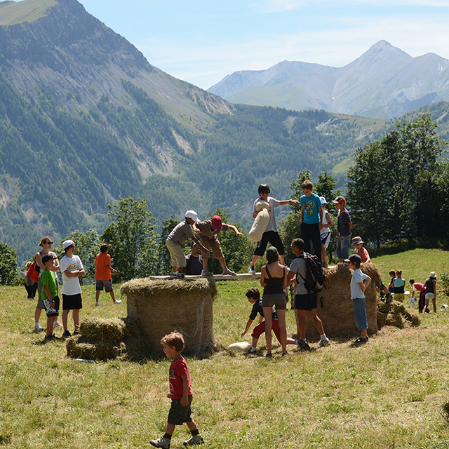 Hooifeest op de alpenweiden van La Toussuire. Een groep kinderen en tieners spelen om zich te laten vallen vanaf een leren zak, gespannen tussen twee ronde hooibalen