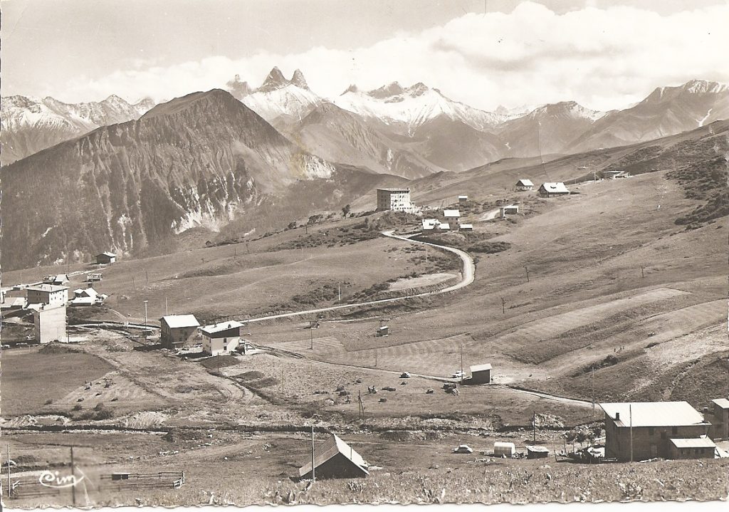 Historical black and white photo of La Toussuire. The photo was taken at altitude, and shows a view of the snow front and the few buildings of the time. Mont-Charvin and Aiguilles d'Arves are in the background