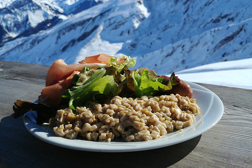 Zoom sur une Croziflette ! Nous pouvons voir un plat de Croziflette avec un doit de Savoie ainsi que de Jambon cru de pays accompagné de salade