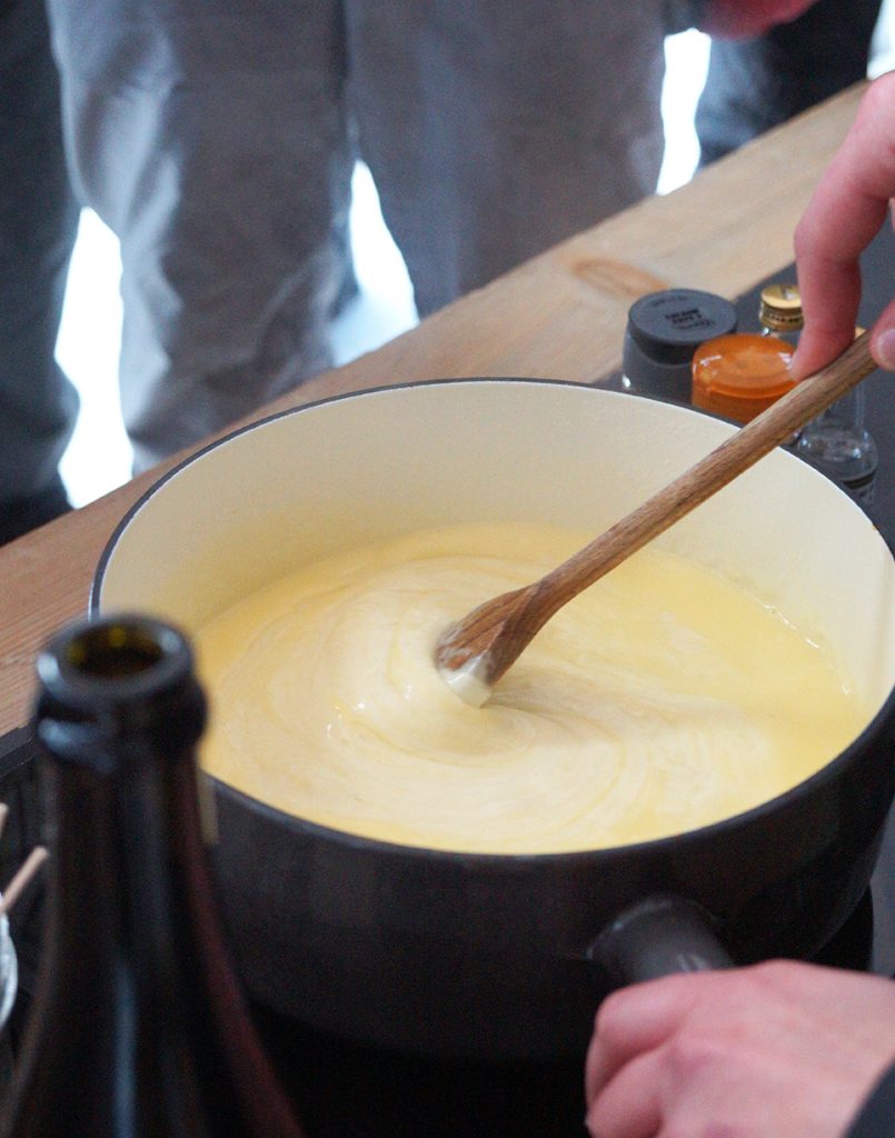 Photo d'une fondue savoyarde. Nous pouvons voir un gros plan sur un appareil a fondue avec quelqu'un qui remue le fromage à l'aide d'une cuillère en bois