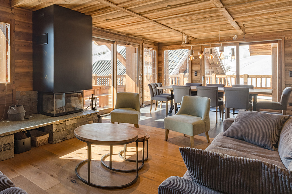 Photo de l'intérieur d'un hébergement. Nous sommes dans pièce de vie salon, salle à manger. Les couleurs et le mobilier sont très chic avec des tons gris et le reste du logement est en bois