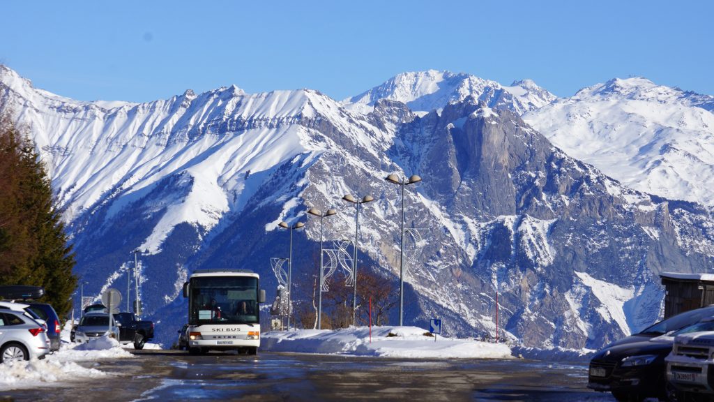 Photo prise en hiver durant une belle journée. Nous voyons le bus de la navette interne entre la Toussuire et le Corbier avec pour fond les montagnes enneigés