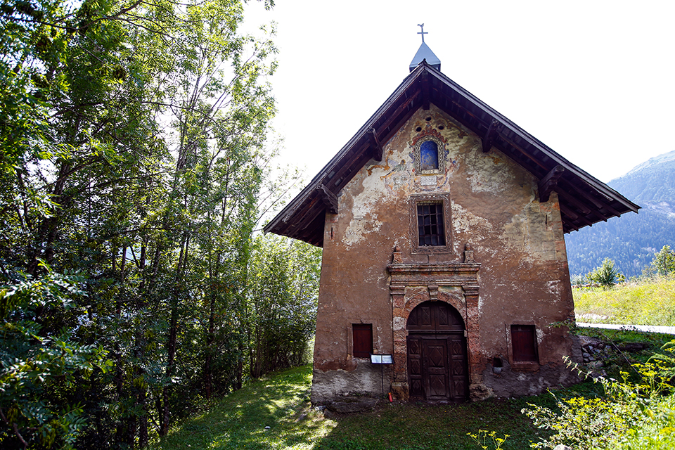Photo de la chapelle des Villard. La photo est prise en journée d'été et nous pouvons voir la façade de la chapelle avec sa porte d'entrée et ses petites fenêtres.