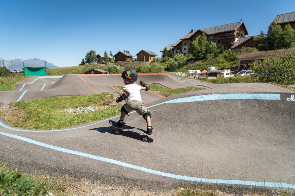 Jeune enfant de dos pratiquant du skateboard sur la pumptrack de la Toussuire