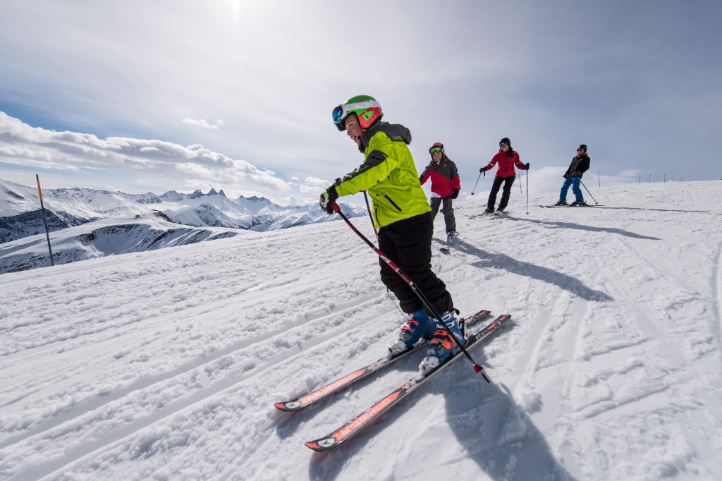 Photo d'une famille en train de faire du ski en hiver. La famille est une sur piste de ski et suivent à la queuleuleu avec le fils au premier plan, la soeur qui suit et les parents à la fin