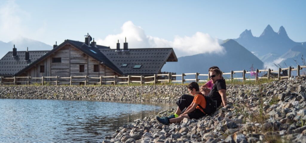 Famille assise sur des cailloux devant le lac de l'Eriscal. Ils sont de profil et avec les Aiguilles d'Arves en fond durant l'été