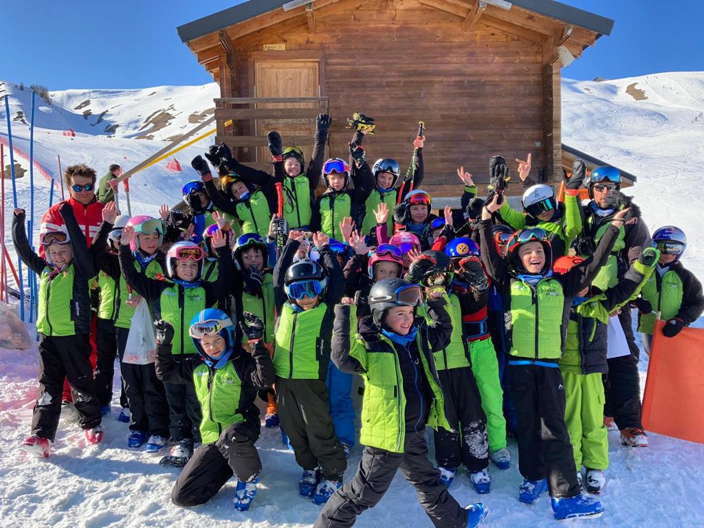 Photo d'un groupe d'enfants du Ski Club de la Toussuire prise de face. Les enfants en tenue de ski prennent la pose pour la photo devant la cabane du chronométrage