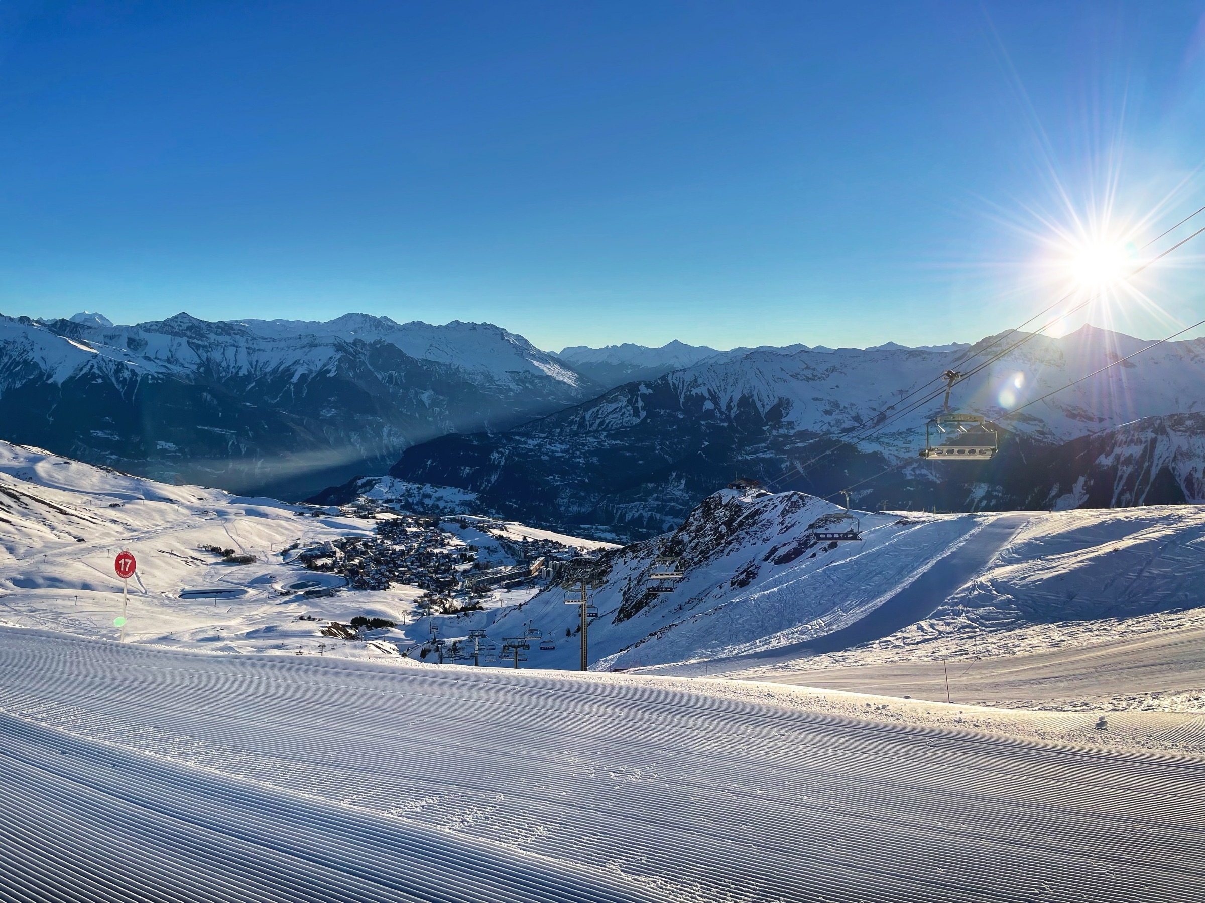 Sunrise photo in the winter. La Toussuire and Maurienne valley seen from Bellard. The foreground shows trails of the famous in the snow, followed by a plunging view of the resort, and the mountains in the background. Beautiful sunlight on the right enhances the scene