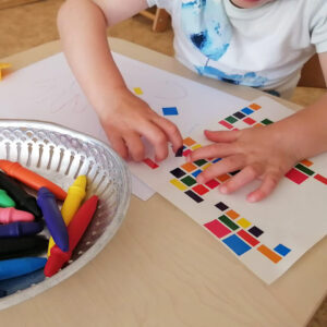 A child playing with stickers and dry pastels. The child is attending daycare at La Ruche children's centre.