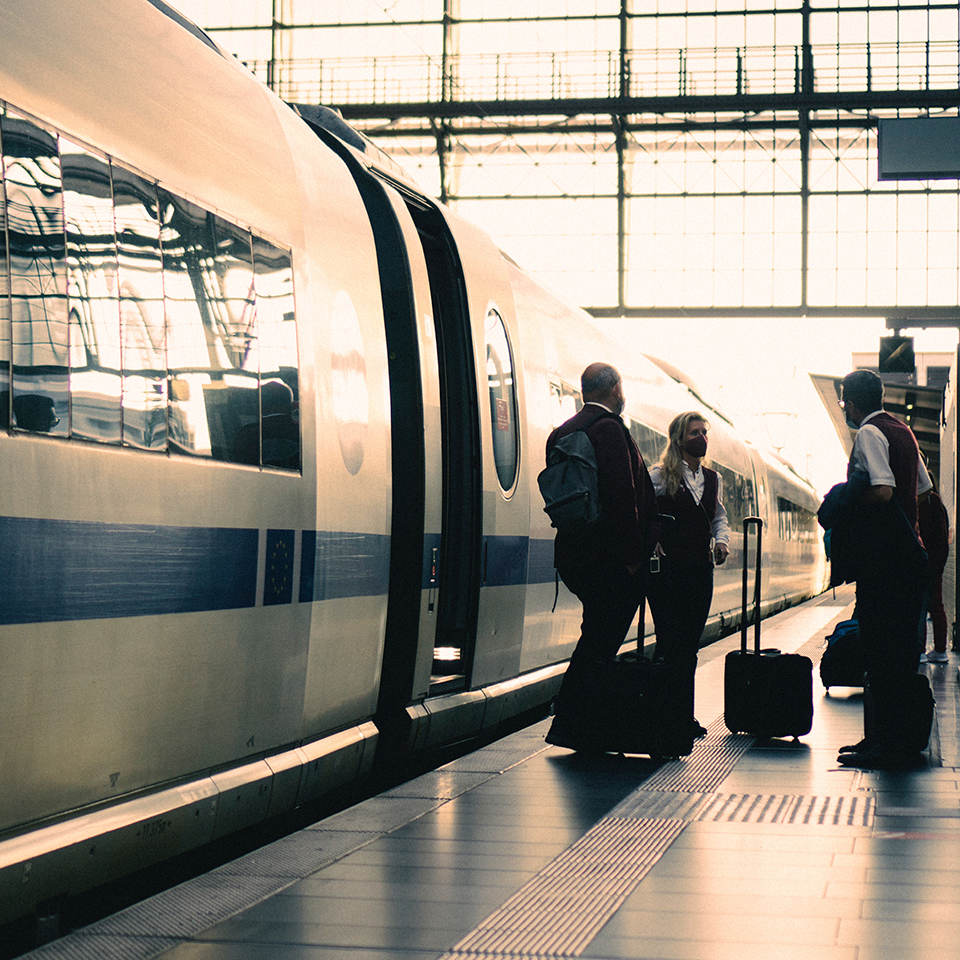 Des voyageurs sur le quai d'une gare près d'un train à l'arrivée. Ils ont des bagages et discutent.