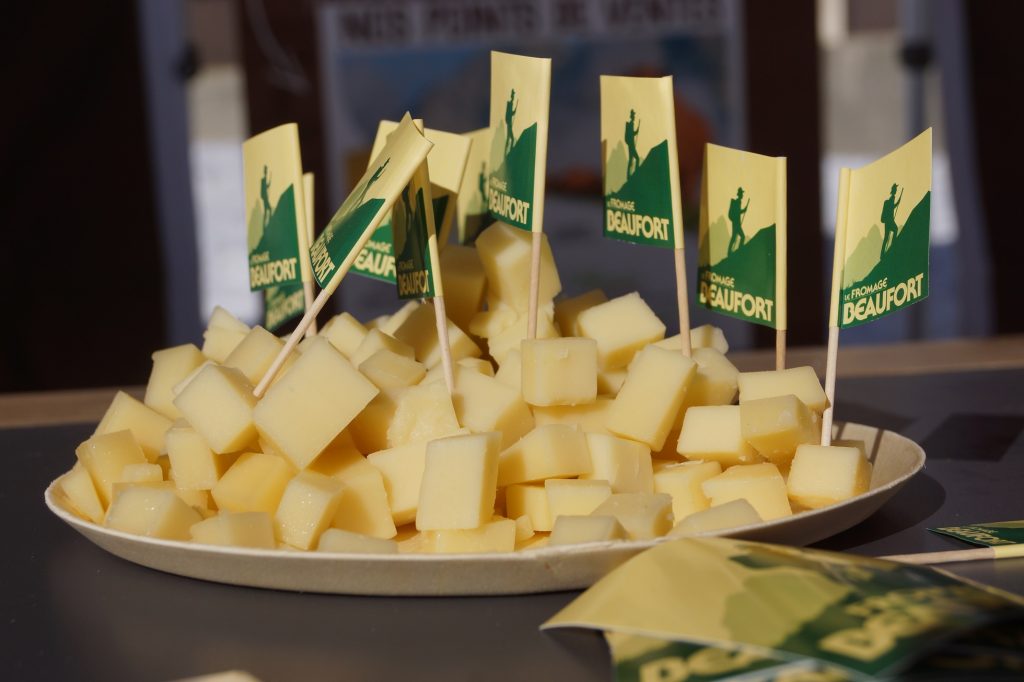 Cubes de fromage de Beaufort plantés de petits drapeaux avec logo Beaufort sur une assiette lors d'une animation gastronomique au soleil sur le front de neige