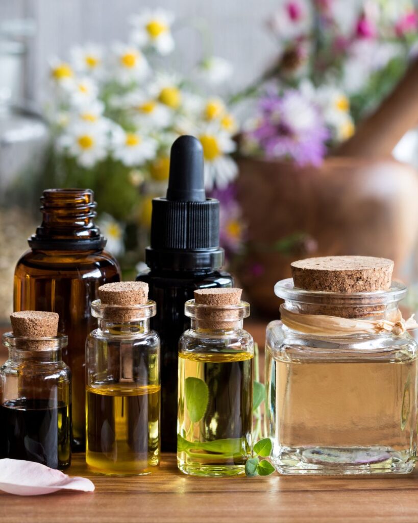 Flacons d’huiles essentielles posés sur un fond naturel, accompagnés d’un diffuseur et de fleurs, un atelier relaxant et sensoriel à retrouver pendant la Semaine Hygge – Bien‑être à La Toussuire.