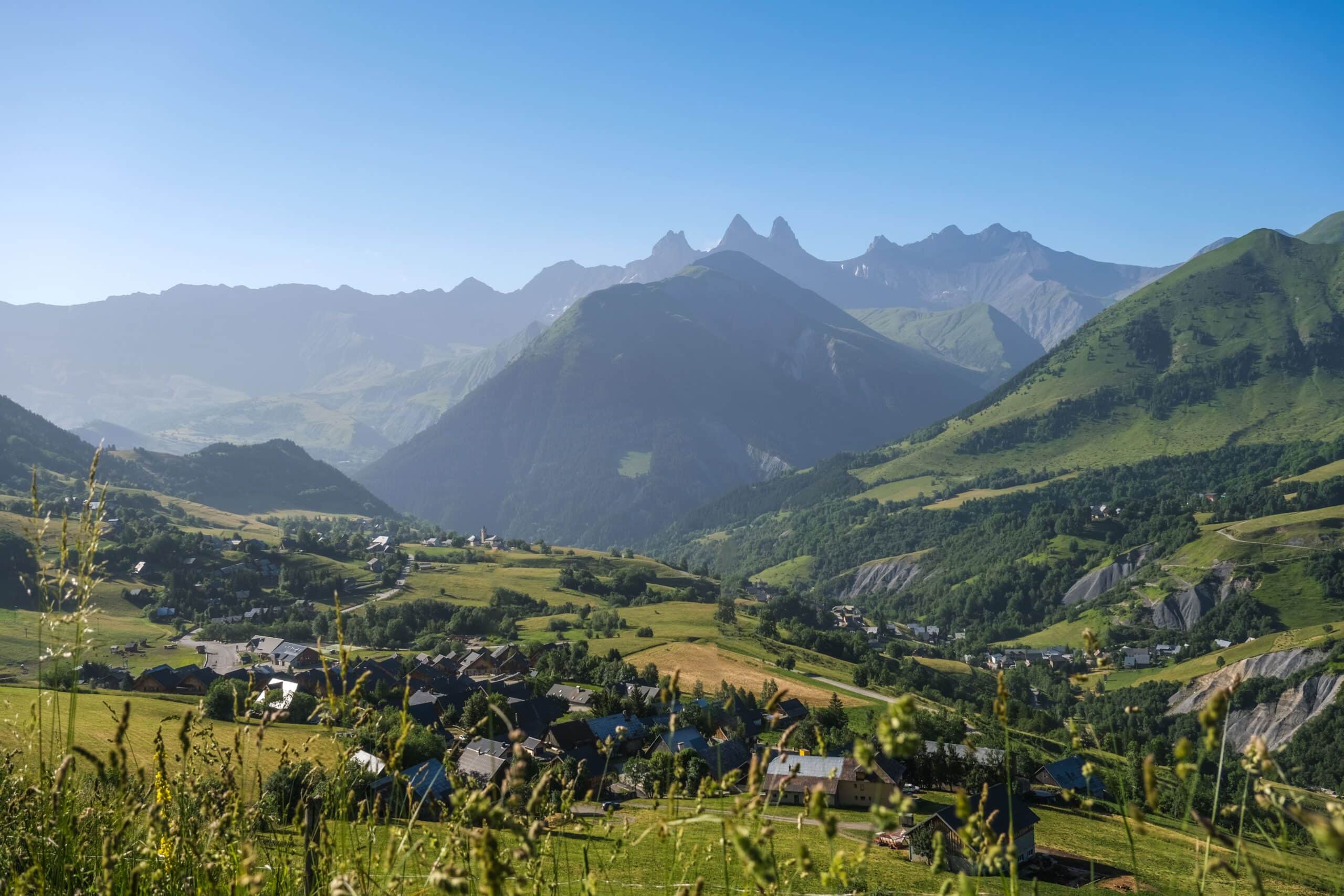 Photo prise de jour en format paysage. Nous pouvons observer la station de saint jean d'arves dans sa globalité. La photo a été prise en été. Nous pouvons également voir les Aiguilles d'Arves en arrière plan